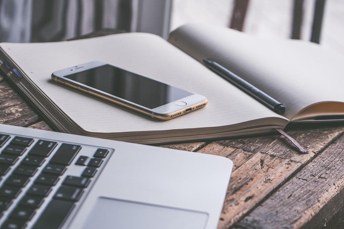 A smartphone, a laptop and a notebook on a wooden desk — every device that goes online is assigned an IP address.