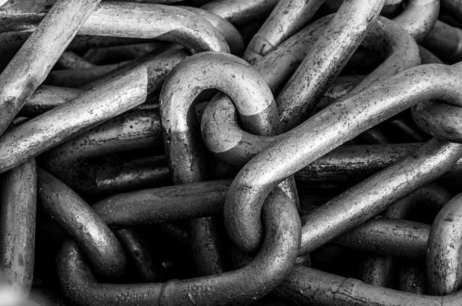 Black and white close-up of a heap of heavy steel chain links, pitted and worn, filling the whole frame.