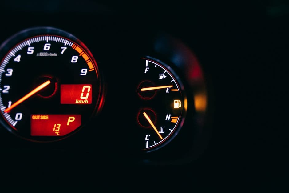 Two illuminated car dials in the dark: a rev counter with its needle at zero showing 0 km/h and an outside temperature of 13 °C, beside fuel and coolant gauges.
