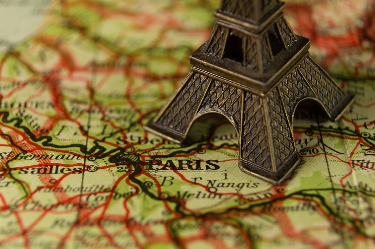 Une figurine en bronze de la tour Eiffel posée sur une carte routière ancienne de la France, avec la mention « PARIS » bien visible.